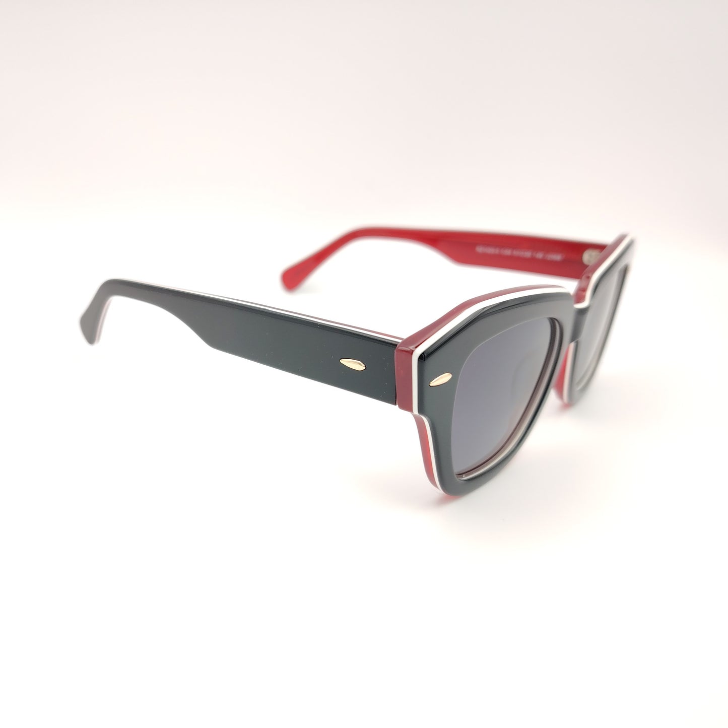 gafas de sol rischio modelo r21423 c04 con montura geométrica en acetato negro con detalles en rojo y blanco, varillas bicolor y lentes polarizadas oscuras