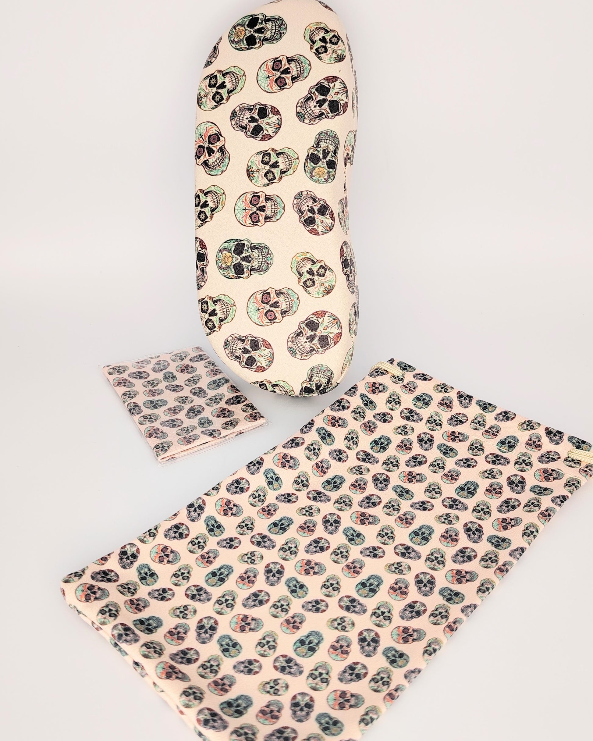 pack para gafas formado por estuche rígido, funda de tela blanda y gamuza limpia gafas, todo ello color beige de fondo en estampado de calaveras multicolor