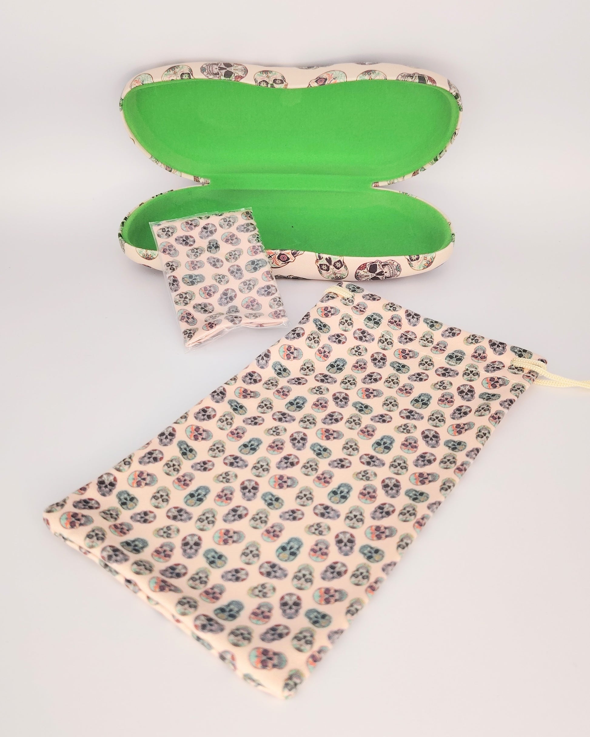 pack para gafas formado por estuche rígido, funda de tela blanda y gamuza limpia gafas, todo ello color beige de fondo en estampado de calaveras multicolor