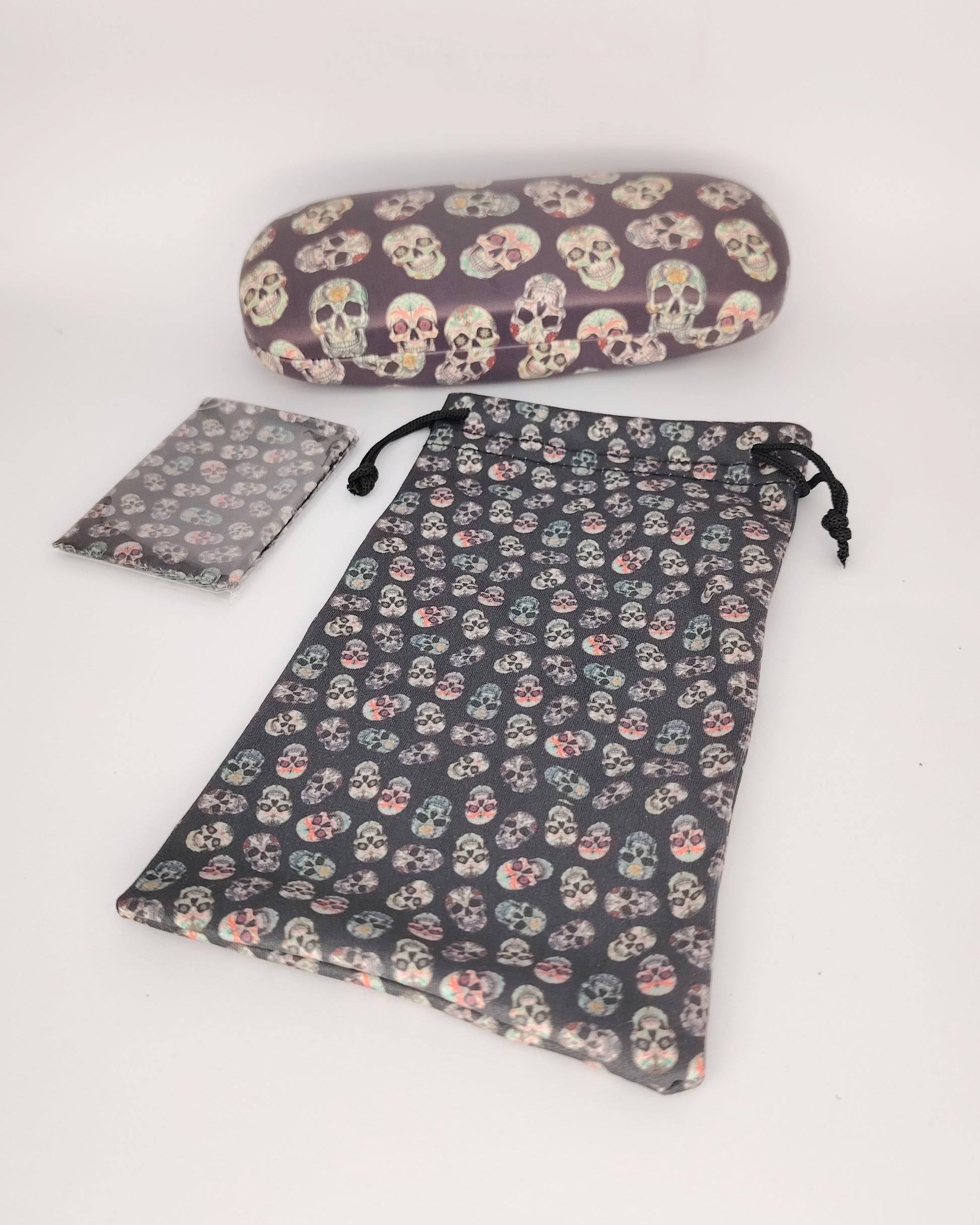 pack para gafas formado por estuche rígido, funda de tela blanda y gamuza limpia gafas, todo ello color negro de fondo en estampado de calaveras multicolor