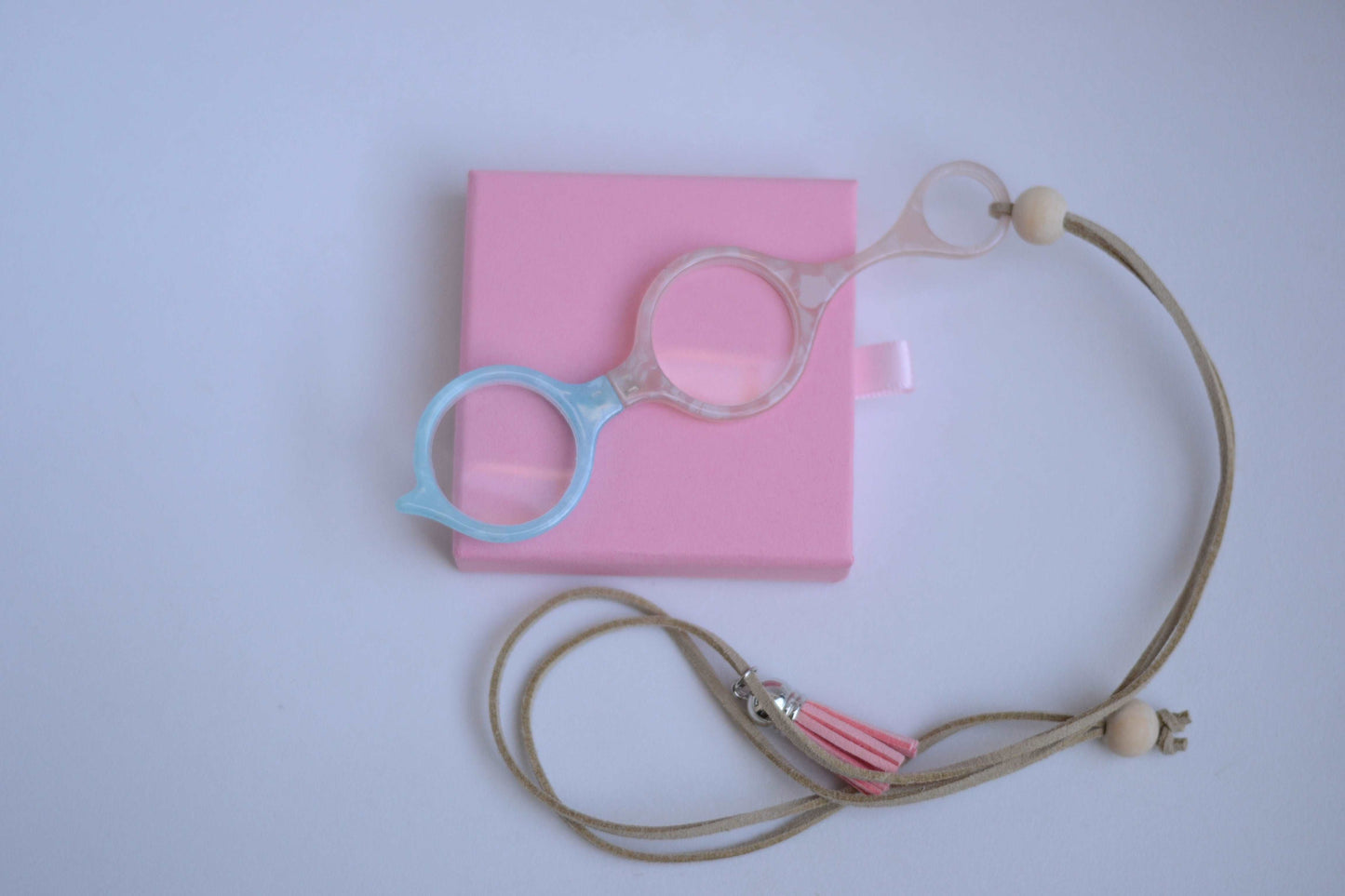 colgante lupa impertilente en tonos beige y azul con correa de cuero abalorios decorativos y borla rosa ideal para llevar siempre a mano con un toque elegante y funciona