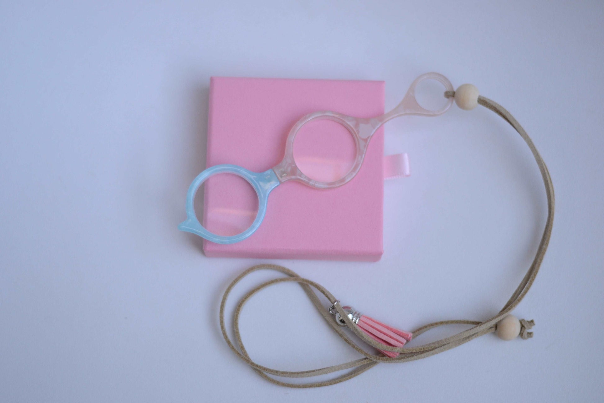 colgante lupa impertilente en tonos beige y azul con correa de cuero abalorios decorativos y borla rosa ideal para llevar siempre a mano con un toque elegante y funciona