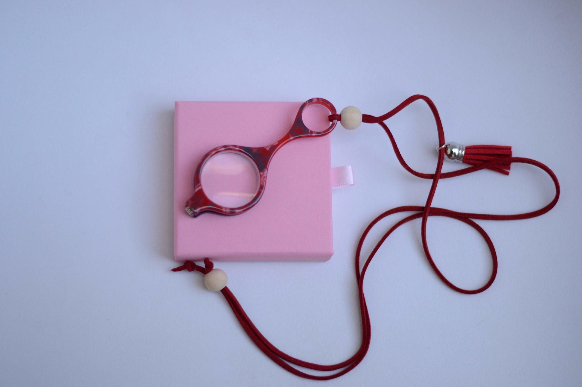 colgante lupa impertilente en combinación de colores rojo y azul con correa de cuero abalorios decorativos y borla roja diseñado para aportar funcionalidad con un toque de estilo